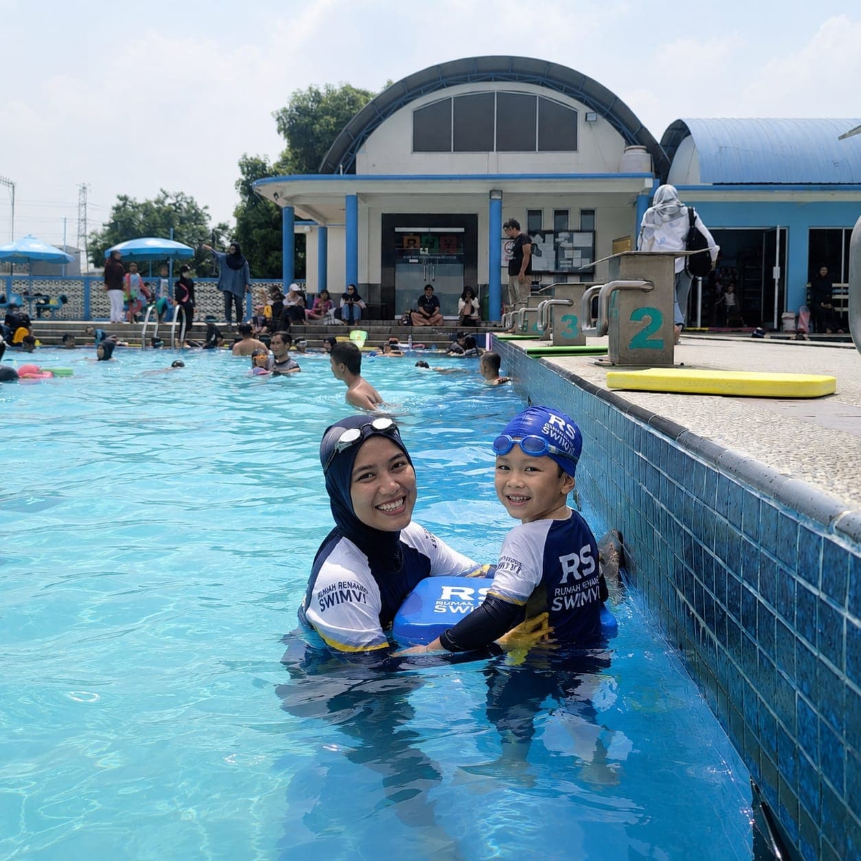 Seorang ibu mendampingi anaknya belajar berenang di kolam Swimvi